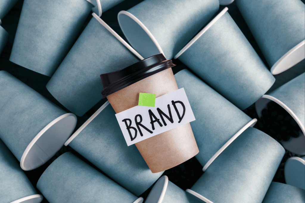 image featured in Your 7-Step Guide to Mindful Consumption | with Helpful Examples + Tips , showing no name coffee cups and one different coloured one that says 'brand'