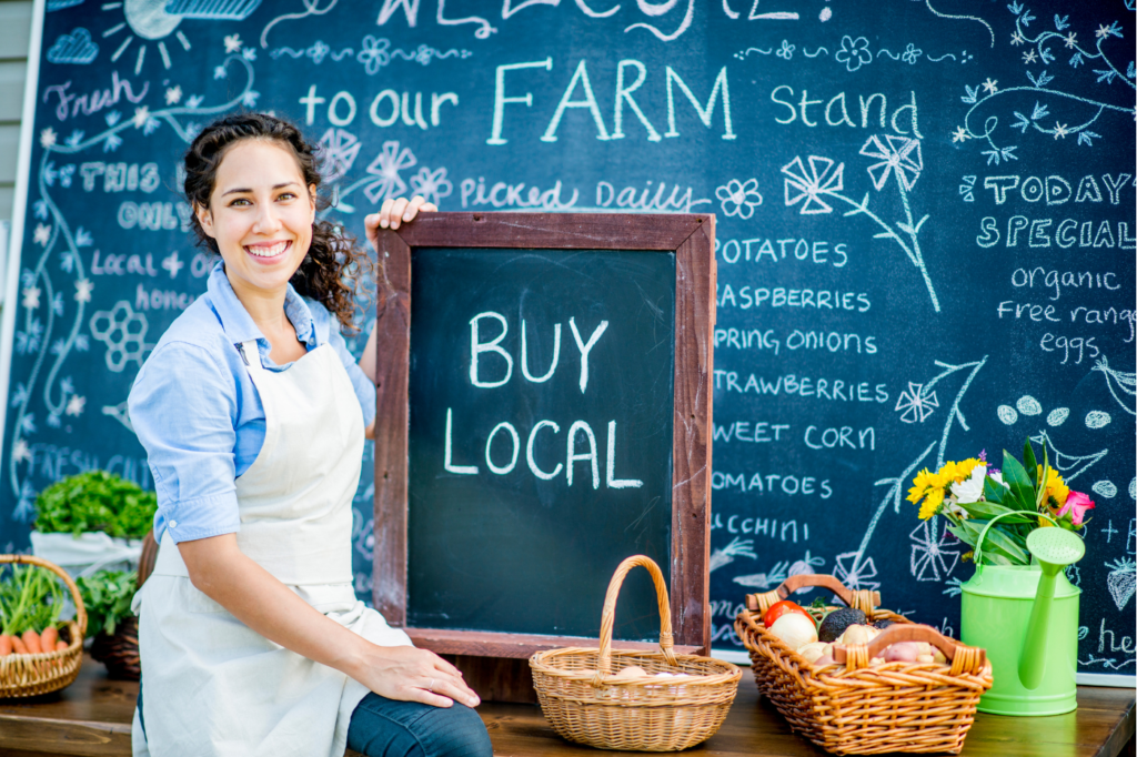 image featured in What is Sustainable Living? Explained With 5 Easy Examples showing a woman holding up a sign that says 'buy local'
