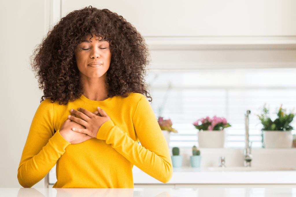 image featured in Your 7-Step Guide to Mindful Consumption | with Helpful Examples + Tips , showing a woman holding her chest with both hands and looking content