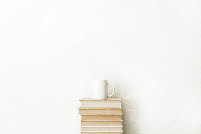 image showing a white wall, in front the wall is a staple of books with a coffee on top symbolizing minimalism